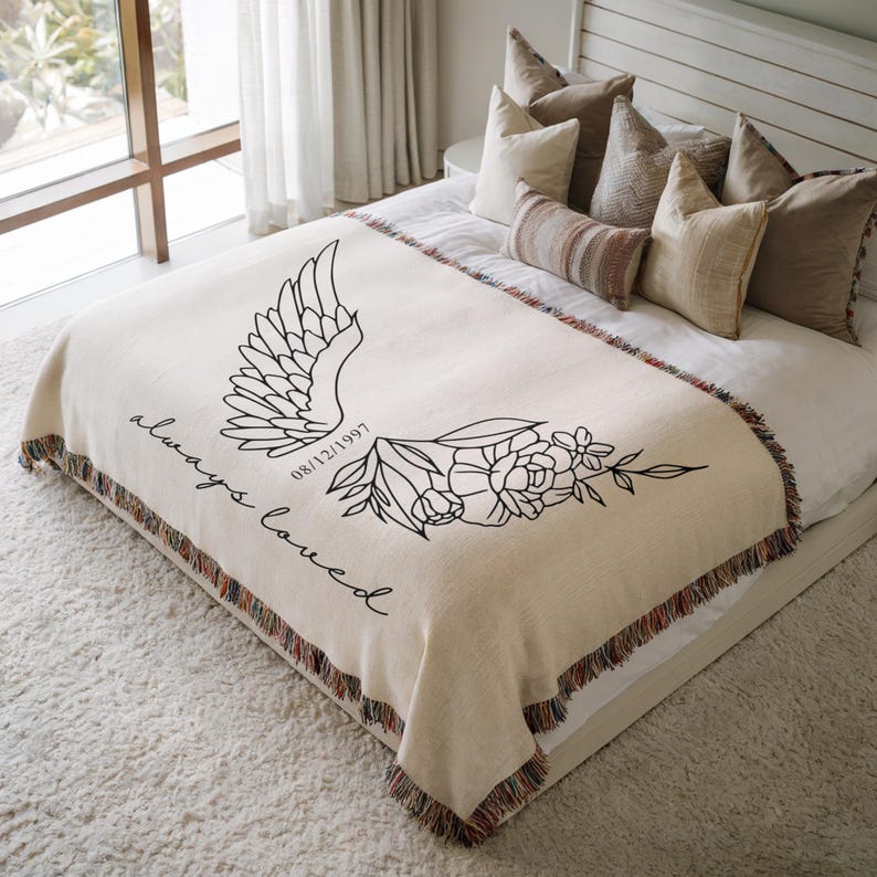 Personalized memorial blanket with angel wings and date on a bed