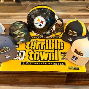 May include: An assortment of Pittsburgh Steelers merchandise, including various baseball caps with the Steelers logo, a black and gold football helmet, and a yellow Terrible Towel. The caps feature different color schemes and patterns.