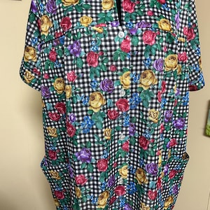 May include: A short-sleeved button-down shirt with a black and white checkered pattern. The shirt is adorned with a floral print featuring yellow, red, purple, and blue roses. It has two front pockets and a collar.