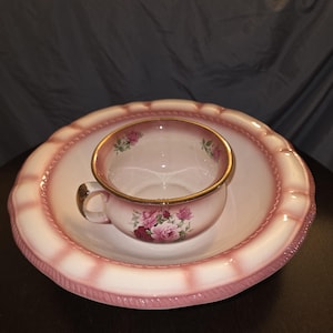 May include: A vintage teacup and saucer set. The cup and saucer are white with pink accents and a gold rim. The cup features a floral design with pink and red roses. The saucer has a scalloped edge.