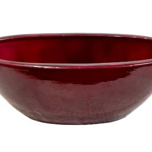 May include: A glossy, oval-shaped bowl in a deep burgundy colour. The ceramic bowl has a smooth, reflective surface and a wide, rounded rim. The bowl is empty and sits against a white background.