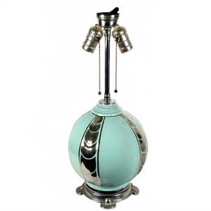 May include: A vintage table lamp with a round, turquoise base and silver accents. The lamp has three light sockets and a silver base with decorative feet. The lamp is approximately 20 inches tall.