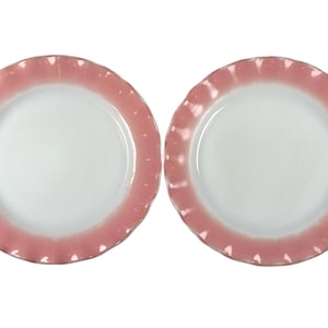 Può includere: Due piatti bianchi con bordo rosa smerlato. I piatti hanno un design semplice ed elegante, con una finitura liscia e lucida. Il bordo rosa aggiunge un tocco di colore e interesse visivo ai piatti.
