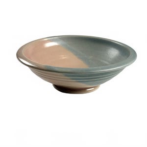 May include: A shallow ceramic bowl featuring a two-tone glaze design. One half of the interior and exterior is finished in a soft, muted pink, while the other half is a dusty blue. The bowl has a wide rim and a circular base with ribbed detailing.