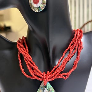May include: A red beaded necklace with a teardrop pendant and matching earrings. The pendant and earrings feature a mosaic design with red, white, and iridescent shell accents. The necklace has multiple strands.