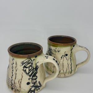 May include: A set of three ceramic mugs with a speckled, matte finish. The mugs are in shades of cream, light gray, and dark gray. Each mug has a simple, minimalist design, perfect for coffee or tea.