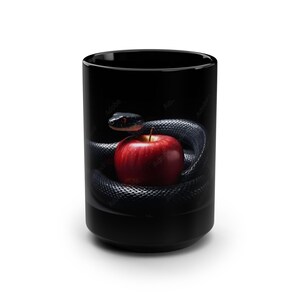 May include: Black ceramic mug with a design of a black snake coiled around a red apple. The snake has a dark head and red eyes. The mug is cylindrical and has a glossy finish.