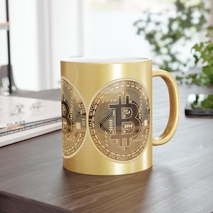 Peut inclure: Mug doré avec un motif Bitcoin. Le symbole Bitcoin est affiché sur la surface de la tasse, avec du texte incluant "Bitcoin Digital Decentralized" et "Fine Copper MIB Monetary Metals". La tasse a une anse dorée.
