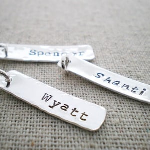 May include: Three silver metal tags with hammered surfaces and personalized names. The names are "Spencer", "Shanti", and "Wyatt".