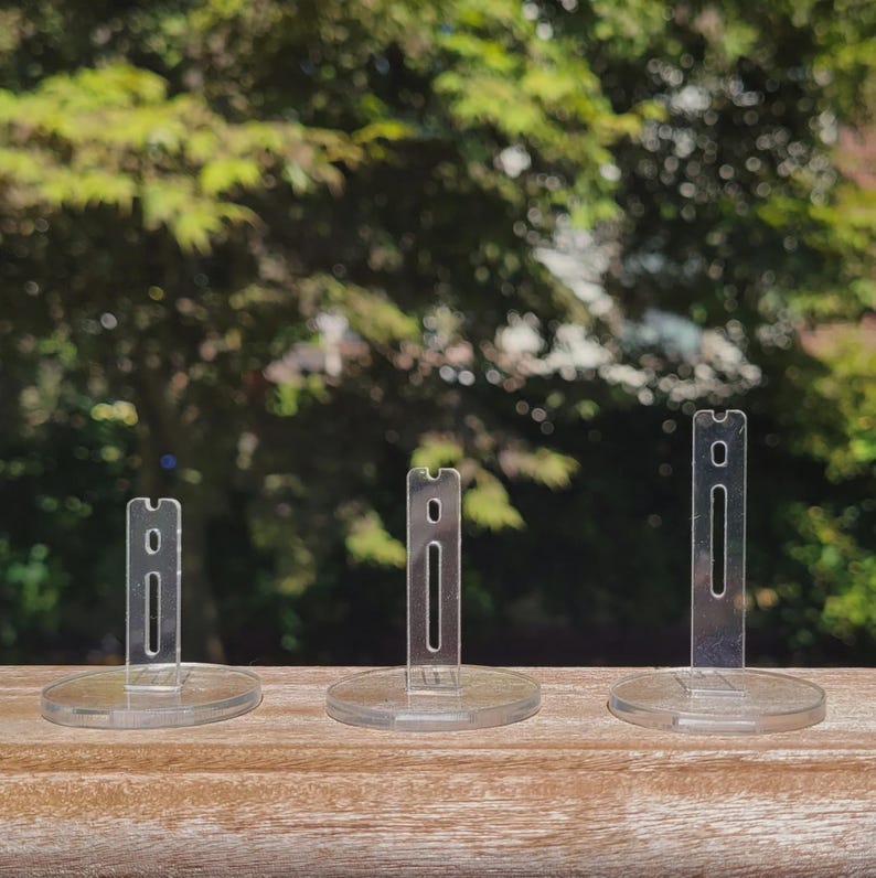 Peut inclure: Trois pr&eacute;sentoirs en plastique transparent de diff&eacute;rentes tailles. Les pr&eacute;sentoirs sont circulaires avec un poteau vertical en plastique transparent au centre.