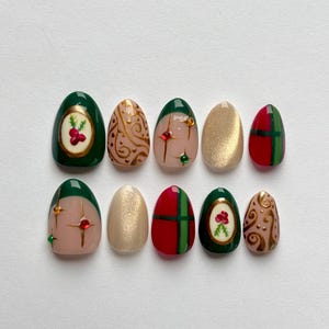 May include: A set of ten artificial nails in various designs. The nails feature colors like green, gold, red, and nude. Some nails have gold swirls, red berries, or a plaid pattern. Others have gem accents.