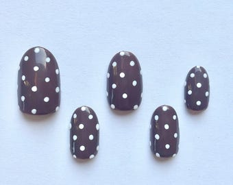 May include: Five oval-shaped false nails with a dark brown base and white polka dots.