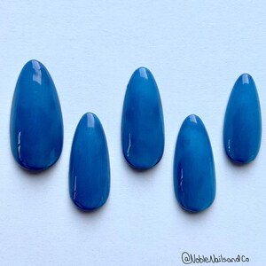 May include: Five blue oval-shaped nail tips, arranged in a row on a white surface.