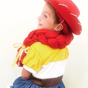 May include: A child dressed as a character from the Toy Story movie franchise. The child is wearing a red cowboy hat, a yellow and white striped shirt, a blue denim skirt, and a red braided scarf.