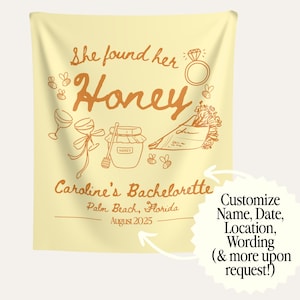 May include: A light yellow tapestry with orange text and illustrations. The text reads "She found her Honey" and "Caroline's Bachelorette" with the location and date. Illustrations include a ring, bees, wine glasses, and a jar of honey.