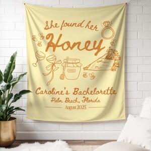 May include: A light yellow tapestry with brown text and illustrations. The text reads "She found her Honey" with a ring, bees, and other illustrations. Below, it says "Caroline's Bachelorette, Palm Beach, Florida, August 2025."