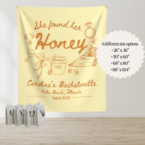 May include: A light yellow bachelorette party tapestry with the text "She found her Honey" and "Caroline's Bachelorette, Palm Beach, Florida, August 2025". The design includes illustrations of a ring, bees, wine glasses, and a honey pot. Four size options are listed.