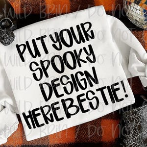 May include: White long-sleeved shirt with the text "PUT YOUR SPOOKY DESIGN HERE BESTIE!" in black. The shirt is folded on a plaid orange and black surface, with a skull and disco ball in the background. Halloween theme.