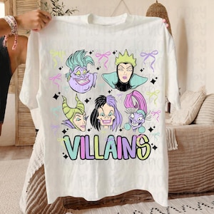 May include: White t-shirt with cartoon illustrations of six villains with colourful hair and makeup. The word "VILLAINS" is printed in pastel colours below the characters. Pastel bows and stars are scattered around the design.