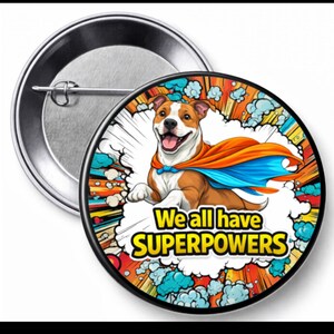 May include: A round button pin featuring a smiling brown and white dog wearing a superhero cape. The pin has the text "We all have SUPERPOWERS" in yellow and white. The background includes clouds and comic book style elements.
