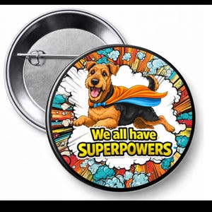 May include: A round button with a cartoon dog wearing a superhero cape. The dog is brown and black with a blue bow tie. The button has the text "We all have SUPERPOWERS" in yellow and white.