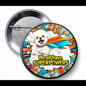 May include: A round button pin with a cartoon illustration of a white dog wearing a superhero cape. The pin has the text "We all have SUPERPOWERS" in yellow and black. The background features colorful comic book style elements.