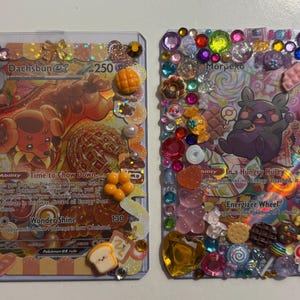 Pode incluir: Duas cartas colecionáveis decoradas. Uma apresenta um personagem Dachsbun com o texto "Time to Chow Down" e "Wonder Shine". A outra carta apresenta um personagem Morpeko com o texto "In a Hungry Hurry" e "Energizer Wheel". Ambas as cartas são adornadas com pedras preciosas coloridas e amuletos temáticos de comida.
