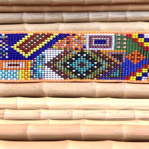 May include: A colorful beaded hair clip with a geometric pattern in shades of blue, red, yellow, green, orange, brown, white, and black.