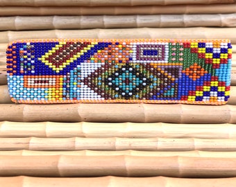 Op de afbeelding: Een kleurrijke kralen haarspeld met een geometrisch patroon in tinten blauw, rood, geel, groen, oranje, bruin, wit en zwart.