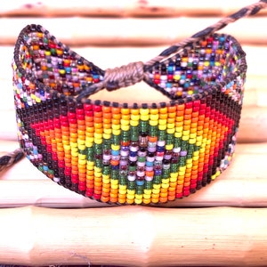 May include: A colorful beaded bracelet with a geometric pattern in shades of red, orange, yellow, green, and blue. The bracelet is tied with a brown cord.
