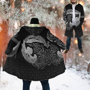 May include: Black hooded cloak with a wolf design in white and gray. The cloak features a geometric pattern at the hem and a faux fur-lined hood. The design is inspired by Norse mythology.