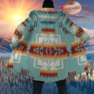 May include: A turquoise hooded cloak with a geometric pattern in shades of red, orange, white, and brown. The cloak has a soft, fuzzy interior and is worn over dark clothing. The background features a mountain range and a sunset.