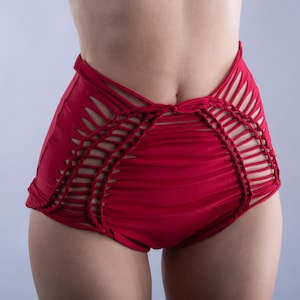 Puede incluir: Pantalones cortos rojos de talle alto con un complejo entramado de aberturas en los laterales. La prenda está confeccionada con un panel frontal sólido y detallados trenzados que conectan las tiras laterales, creando una serie de aberturas horizontales.