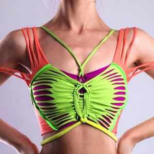 May include: A vibrant crop top in neon green and purple, featuring a distinctive cut-out pattern. It has orange straps and a yellow waist band. The design incorporates a woven detail at the centre.