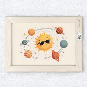 Op de afbeelding: Een ingelijste print met een cartoon illustratie van de zon met een zonnebril, omringd door planeten in tinten oranje, blauw en bruin. De achtergrond is lichtbeige en het frame is van licht hout.