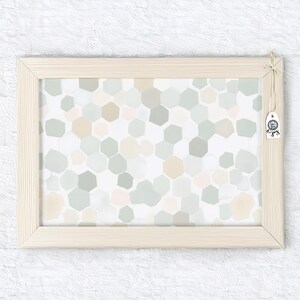 May include: A framed print with a light wood frame. The artwork features a pattern of irregular, pastel-colored hexagons in shades of green, beige, and pink on a white background. A small tag is attached to the frame.