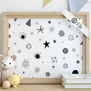 Op de afbeelding: Een houten lijst met een witte achtergrond met zwarte geometrische vormen en sterren. Een wit lint met de tekst "O Joy" is over de lijst gedrapeerd. Een knuffel en twee boeken staan voor de lijst.