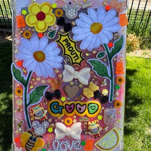 May include: A pink iPad case with a glittery background and various colorful embellishments, including flowers, bows, and cartoon characters. The text "PROUTI" and "GROOVY" are visible on the case.