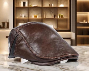 May include: A brown leather flat cap with a curved brim. The cap has a stitched design and a black accent on the side. The cap is sitting on a marble surface. The text "JavaBeautyID" is at the bottom.