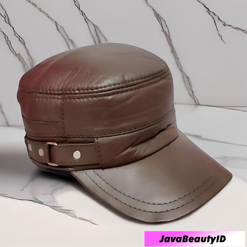 K&ouml;nnte beinhalten: Braune Milit&auml;r-Cap aus Leder mit kurzem Schirm. Die Cap hat ein dekoratives Band mit Schnalle und besteht aus glattem, gl&auml;nzendem Material. Die Cap ist neutralfarben und hat ein klassisches Design.