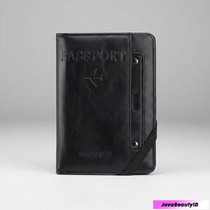 May include: Black passport holder with embossed text "PASSPORT" and an airplane symbol. The holder has a strap closure and the text "SHINING STAR" at the bottom. The design is sleek and minimalist.