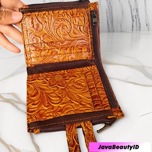 May include: Open, brown leather wallet with a floral embossed pattern. The wallet features multiple card slots, a zipped compartment, and a brown zip closure. The wallet is open, revealing the interior.
