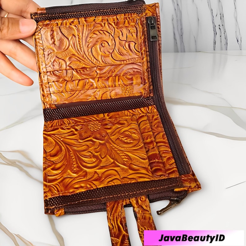 May include: Open, brown leather wallet with a floral embossed pattern. The wallet features multiple card slots, a zipped compartment, and a brown zip closure. The wallet is open, revealing the interior.