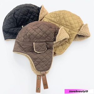 May include: Three quilted trapper hats in black, brown, and tan. Each hat features a diamond pattern, faux fur lining, and ear flaps. Brown hat has a small pocket and leather chin straps with metal snaps.