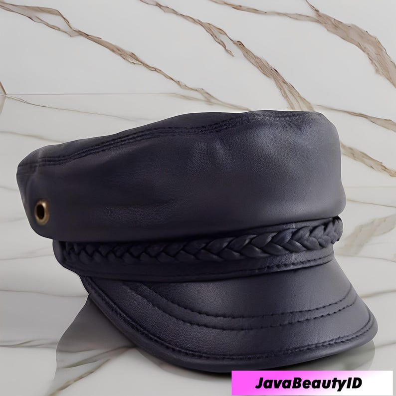 K&ouml;nnte beinhalten: Marineblaue Lederkappe mit geflochtenem Band und kleinem Schirm. Die Kappe hat ein gen&auml;htes Design und eine kleine goldfarbene &Ouml;se an der Seite. Der Text "JavaBeautyID" ist unten im Bild sichtbar.