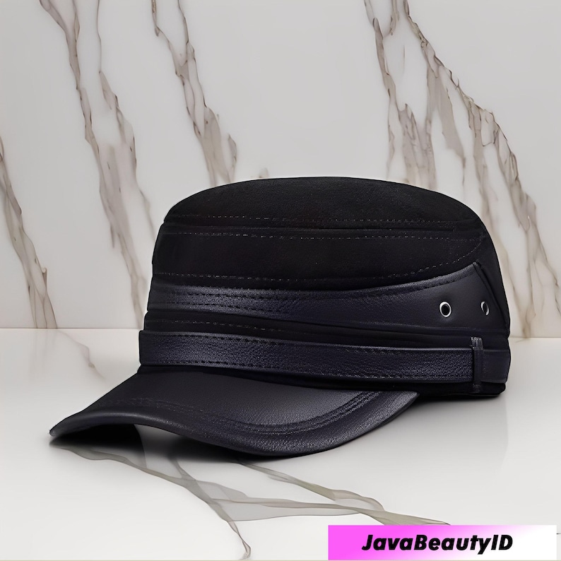 May include: A black military-style cap with a flat brim. The cap features a dark blue leather band and brim, with two small metal eyelets on the side. The top of the cap has a textured, suede-like appearance.