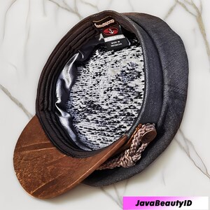 May include: A dark gray newsboy cap with a brown, textured brim. The interior features a patterned lining and a tag that reads "SEAHAMWOOD". A decorative rope detail is attached to the side.