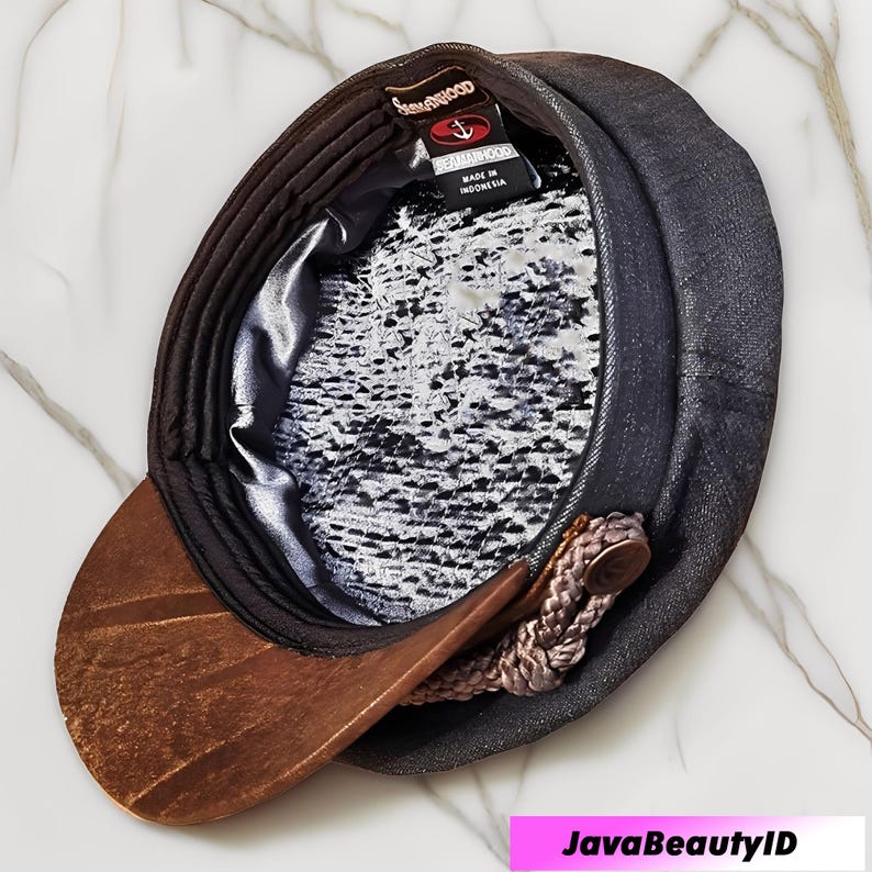 May include: A dark gray newsboy cap with a brown, textured brim. The interior features a patterned lining and a tag that reads "SEAHAMWOOD". A decorative rope detail is attached to the side.