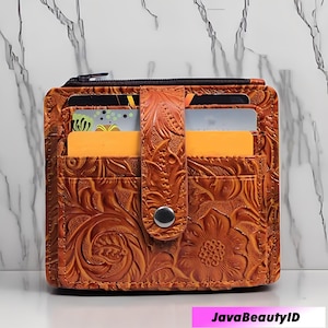 May include: A brown leather wallet with a floral embossed design. The wallet has multiple card slots and a zippered compartment. A snap closure secures the flap. The text "JavaBeautyID" is at the bottom.