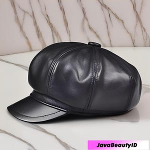 May include: A black leather newsboy cap with a rounded crown and a short, stiff brim. The cap has a glossy finish and is set against a marble background. The text "JavaBeautyID" is visible in the bottom right corner.